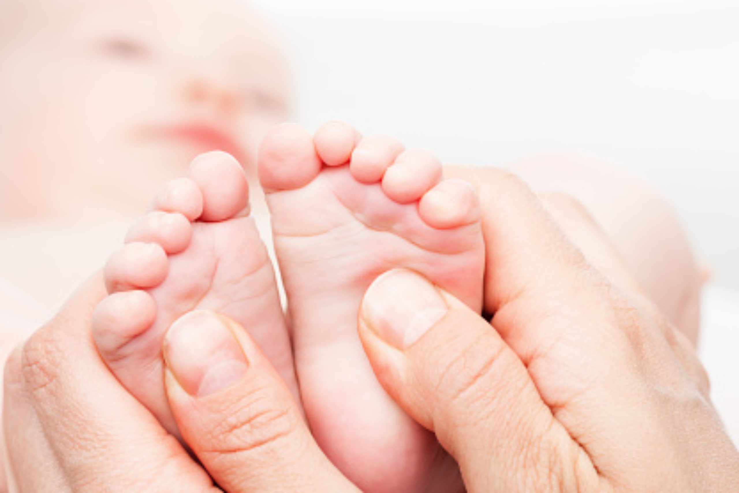 Close-up shot of three month baby girl's foot manipulated by osteopathic manual therapist or physician